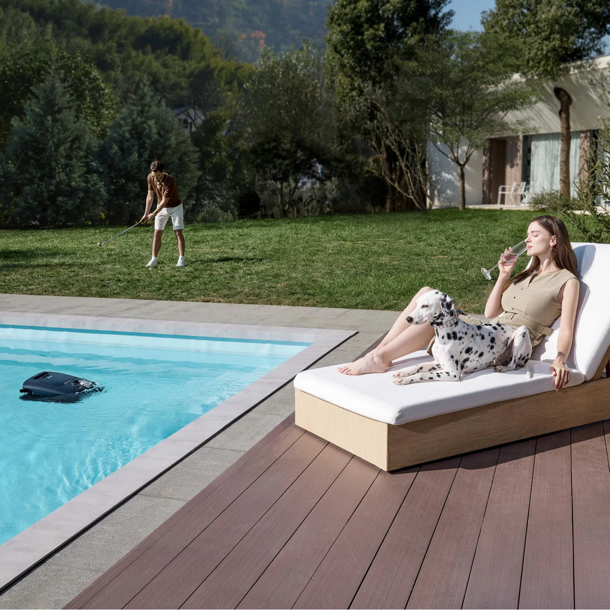 Robotic pool cleaner floating in a clear pool beside a woman on a lounger and a dog