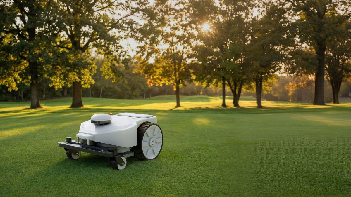 FJD FRX robotic mower on a tree-lined golf course at sunrise